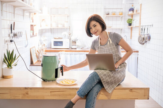 Portrait of asian chef girl cooking potato fried by Air Fryer machine in kitchen home. New normal work at home lifestyle. Technology eco friendly home smart device, asian housewife, minimal concept