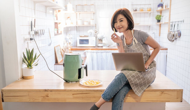 Portrait Of Asian Chef Girl Cooking Potato Fried By Air Fryer Machine In Kitchen Home. New Normal Work At Home Lifestyle. Technology Eco Friendly Home Smart Device, Asian Housewife, Minimal Concept