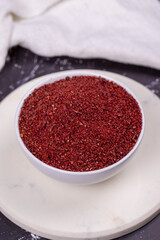 Obraz na płótnie Canvas Sumac on dark background. Dried ground red Sumac powder spices in wooden bowl. Close up