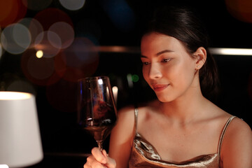 Beautiful woman in elegant golden dress holding red wine in luxury bar on rooftop of city hotel.