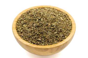 Dried crushed basil isolated on white background. Dried ground basil powder spices in wooden bowl. Spice concept