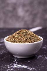 Dried crushed basil on dark background. Dried ground basil powder spices in ceramic bowl. Spice concept. Close up