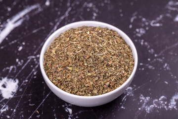 Dried crushed basil on dark background. Dried ground basil powder spices in ceramic bowl. Spice concept. Close up