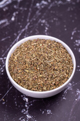 Dried crushed basil on dark background. Dried ground basil powder spices in ceramic bowl. Spice concept