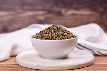 Dried crushed basil on wooden background. Dried ground basil powder spices in ceramic bowl. Spice concept