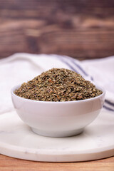 Dried crushed basil on wooden background. Dried ground basil powder spices in ceramic bowl. Spice concept. Close up