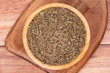 Dried crushed basil on wooden background. Dried ground basil powder spices in wooden bowl. Spice concept. Top view