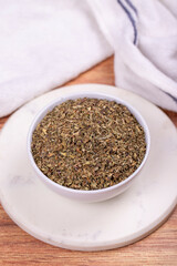 Dried crushed basil on wooden background. Dried ground basil powder spices in ceramic bowl. Spice concept. Close up