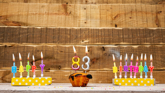 83 Muffin with a burning candle background for the anniversary on a beautiful wooden background. Postcard with letters of candles with congratulations for the holiday before the birthday.