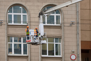 Cleaning team in aerial platform washing window and facade of historic building. Utility men in...