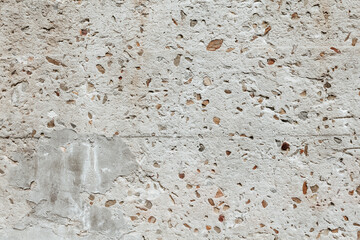 Fragment of an old wall with damages and little rocks. Grunge texture close up. Stone wall background.