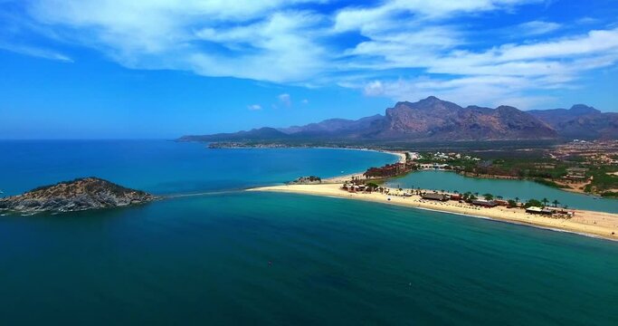 Stationary Aerial Over Blue Bay with Resorts, Beach and Distant Mountains