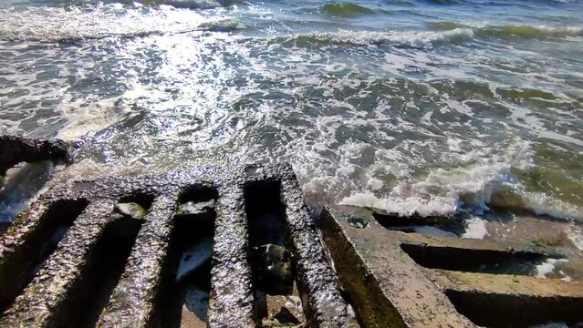 Sea waves beat against old concrete stone slabs on shore on sunny summer day. Blue sea waves with white foam rolling. Seascape landscape. Seaside seashore shoreline. Natural background nature backdrop