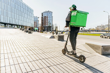 A man on an electric scooter with a thermo backpack is a courier service employee delivering an...