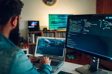 A database scientist is entering data on his laptop while sitting in a home office surrounded by screens.
