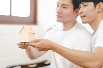 Asian Gay Couple Buying New Dream House Or Property with house model. Concept for marriage, loan, finance, insurance, mortgage, real estate and property.