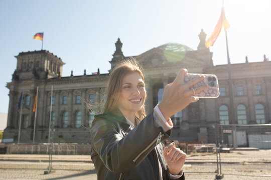 Young woman taking a selfie in front of the German Parliament on her sightseeing tour in Berlin, Germany. Bundestag.