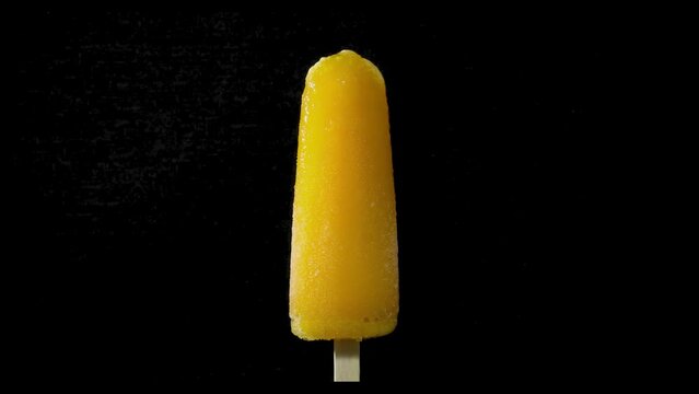 Helado polo de naranja derriti&eacute;ndose a c&aacute;mara r&aacute;pida en fondo negro