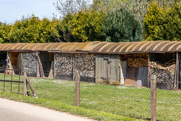 Rural scene of pile of chopped pieces of firewood stacked in rustic shed on a farm, leafy pine...
