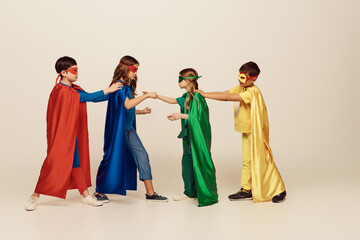 side view of interracial kids in colorful superhero costumes with masks and cloaks fighting with...