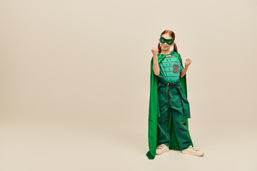 powerful girl in green superhero costume with cloak and mask on face, wearing pants and t-shirt and...