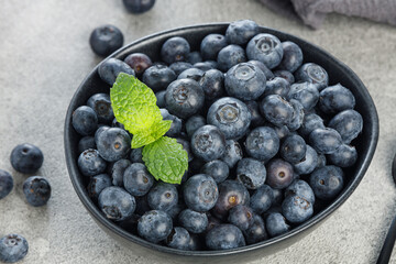 Natural blueberries in a black bowl with mint on gray background, macro