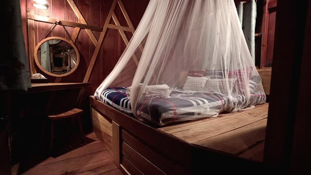 Comfortable bed with mosquito net on wooden platform in cozy cabin.