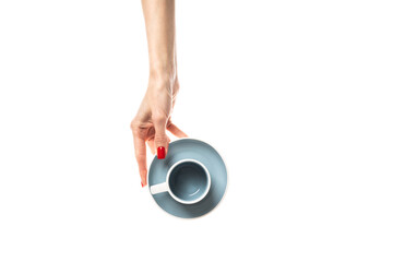 Female hands hold a white ceramic cup with a saucer on white background. Female hands with fresh red manicure. Isolated on white background.