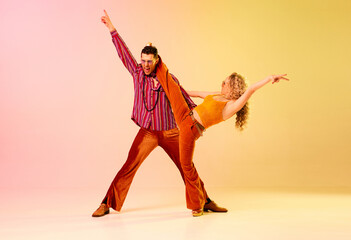 Artistic, talented ,emotional young people, man and woman in stylish clothes dancing disco dance against gradient pink yellow background. Concept of retro style, dance, fashion, art, hobby, music, 70s