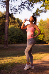 Young woman drinking water after exercise in summer nature