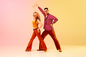 Artistic, expressive man and woman in stylish clothes dancing disco, retro dance against gradient pink yellow background. Concept of retro style, dance, fashion, art, hobby, music, 70s, hobby