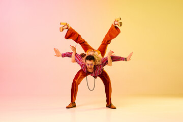 Dynamic image of artistic, beautiful couple, man and woman in stylish clothes dancing against gradient pink yellow background. Concept of retro style, dance, fashion, art, hobby, music, 70s
