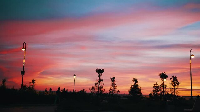 Beautiful pink sunset in the city park, silhouettes of people walking in the evening