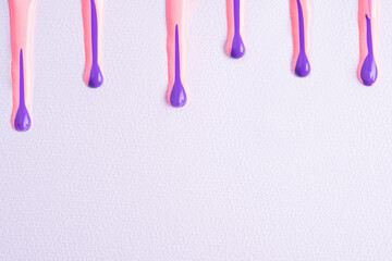 Pink and purple liquid drops of paint color flow down on white paper. Abstract art. Colorful paint dripping on the white with copy space..