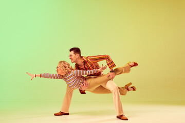 Stylish, expressive, talented young man and woman in vintage clothes dancing against gradient green...