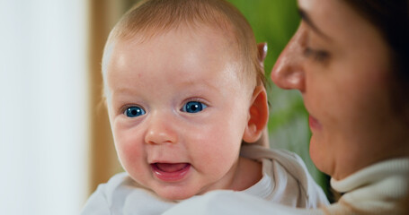 Close-up of young caucasian mother who carries the infant in her arms, little boy with blue eyes lies in his mother's shoulder, son hugs mom