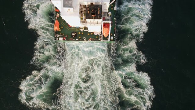 Aerial view of a container ship sails on the sea, its massive hull slicing through the water as it carries cargo across the world. The ship is surrounded by endless waves
