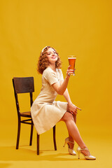 One young beautiful girl wearing stylish retro clothes holding big beer mug and smiling over yellow background. Fresh hop beer
