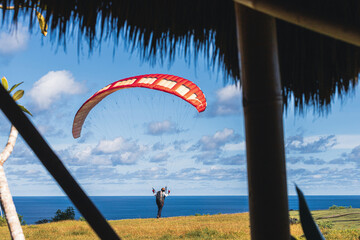 Red paraglider against the blue sky and ocean