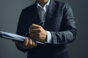 Man holding clipboard and writing to the paper on the dark background.
