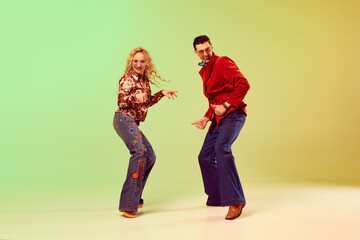 Young emotional couple, man and woman in stylish retro clothes dancing against gradient green...