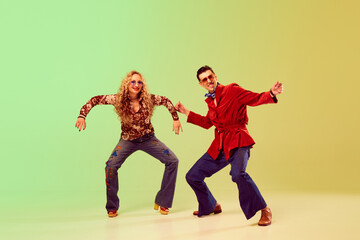 Young emotional couple, man and woman in stylish retro clothes dancing against gradient green yellow background. Concept of retro style, disco dance, fashion, art, hobby, music, 70s
