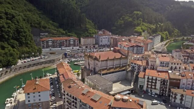 Aerial pan reveals green wide winding canal and beautiful spanish architecture of coastal buildings in ondarroa