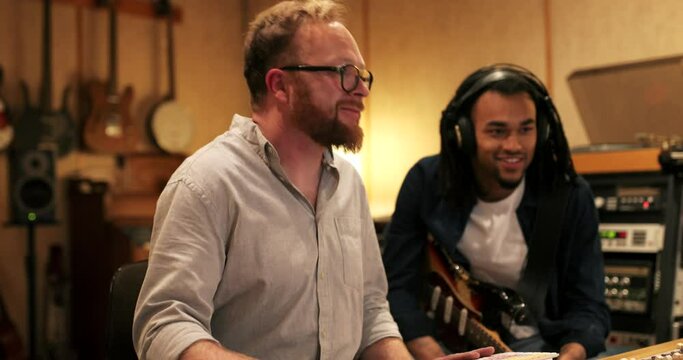 Young African American guitarist and music producer working on a track together during a session in a recording studio