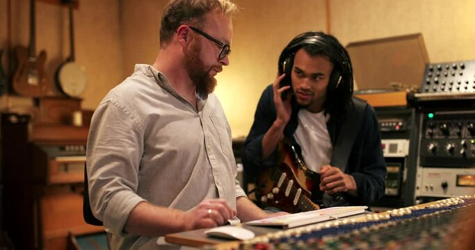 Young African American guitarist and music producer working on a track together during a session in a recording studio