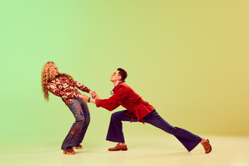 Young handsome man and beautiful woman in stylish retro clothes dancing against gradient green...