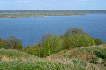 Fototapeta na wymiar A blue lake and a hill with trees and a coastline with forest in the background