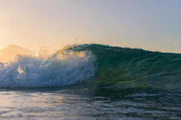 A big wave breaking under the sunset light.