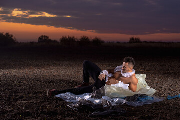 sports man with athletic figure wrapped in plastic on the ground at sunset, garbage problem, environmental disaster, land pollution