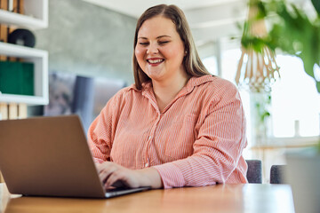 A smiling curvy businesswoman having an online meeting on a laptop with colleagues from work.